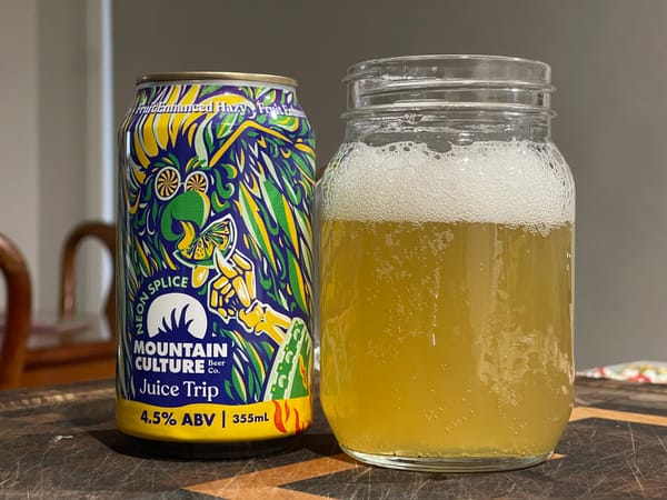 A brightly coloured beer can sitting on a table next to a mason jar full of piss-coloured liquid. The liquid is beer.